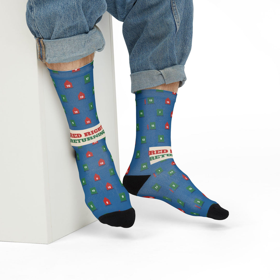 Seated model in rolled jeans leaning on a white block in blue buoy socks with red and green slogan band