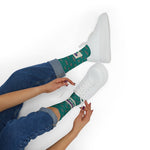 Seated model lacing white sneakers in Quahog Squad Rhode Island clam socks, black jeans rolled above the cream band