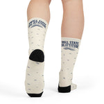 Model mid-step from behind showing the black heel of white Small State. Big Attitude. Rhode Island gift socks