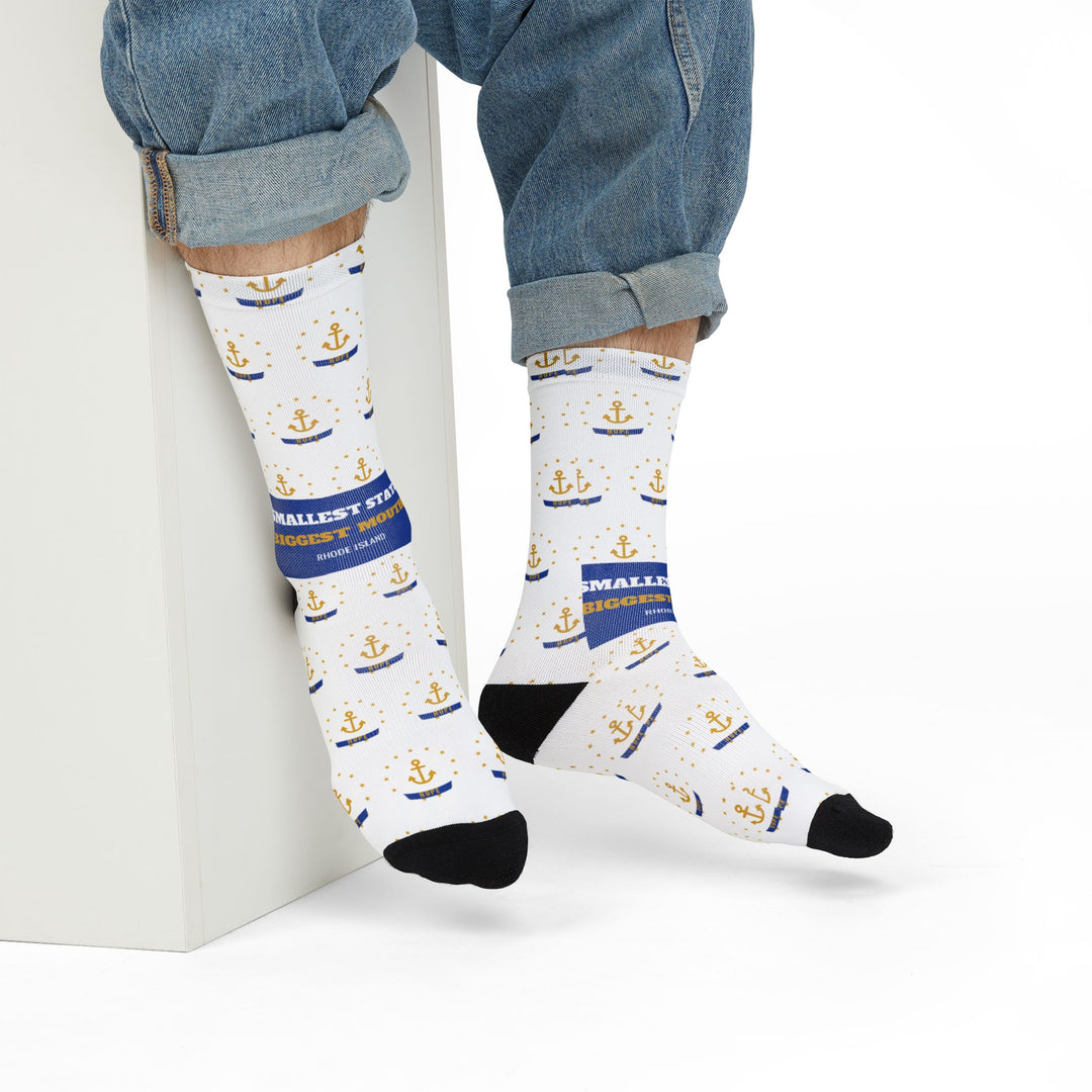 Model in rolled jeans seated on a white block wearing white Rhode Island socks with blue Biggest Mouth band
