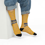 Model in rolled jeans seated on a white block wearing mustard yellow Rhode Island hot wiener socks