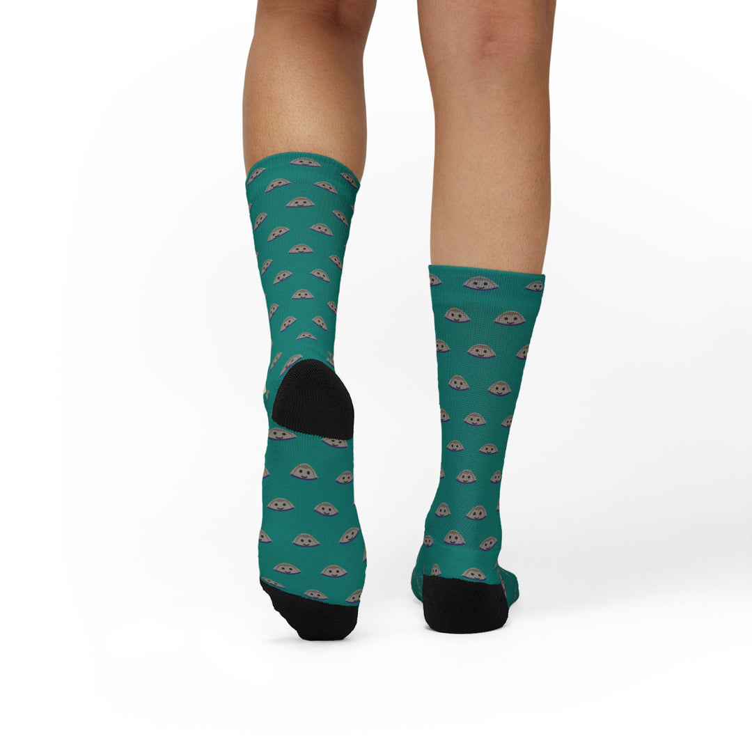 Rear view of a model's calves in teal Quahog Squad funny beach socks, black heel cups against the clam shell print