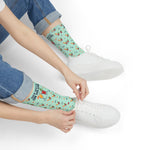 Seated model in rolled jeans pulling on mint green Block Island cocktail socks next to white sneakers