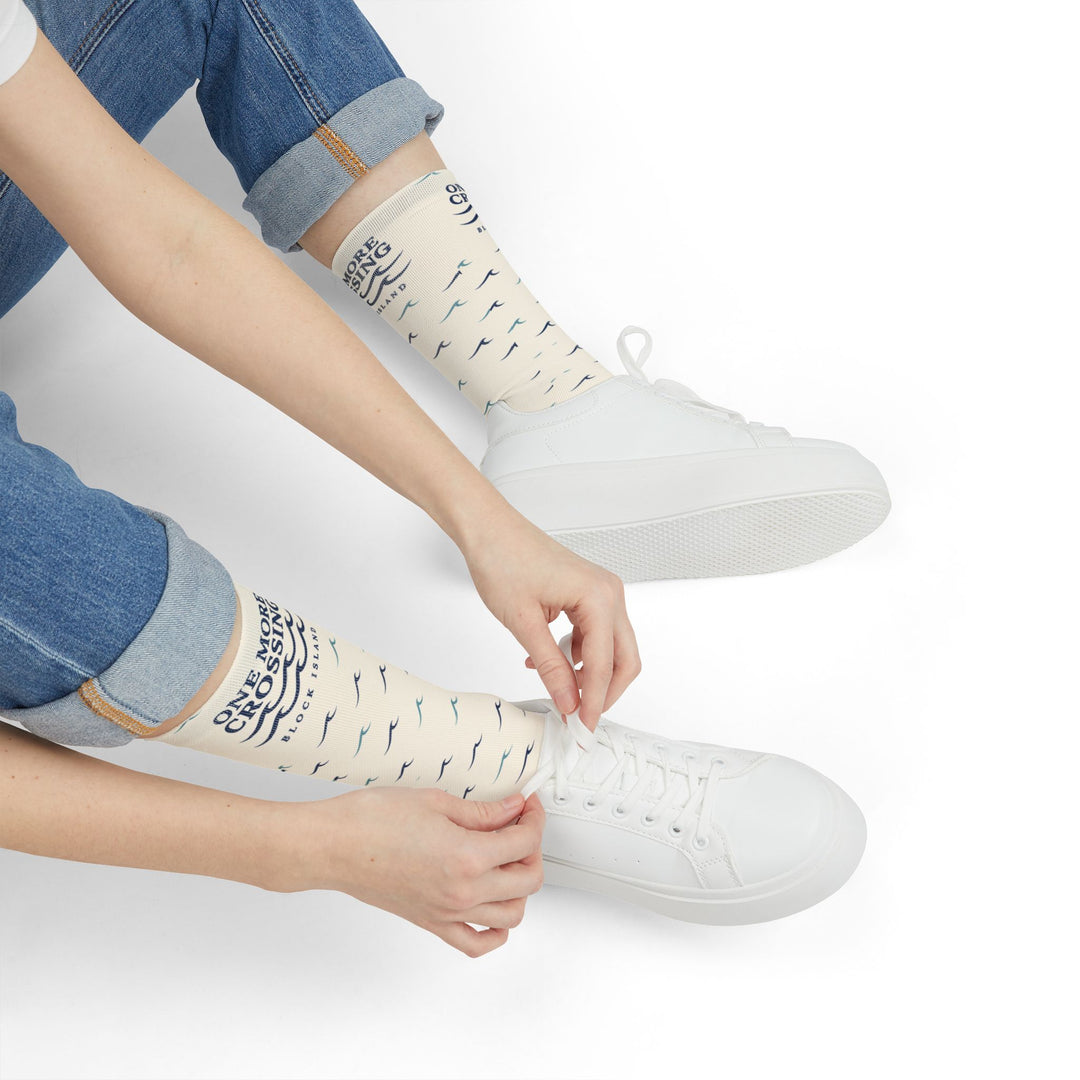Seated model in rolled jeans pulling on One More Crossing nautical crew socks beside white sneakers