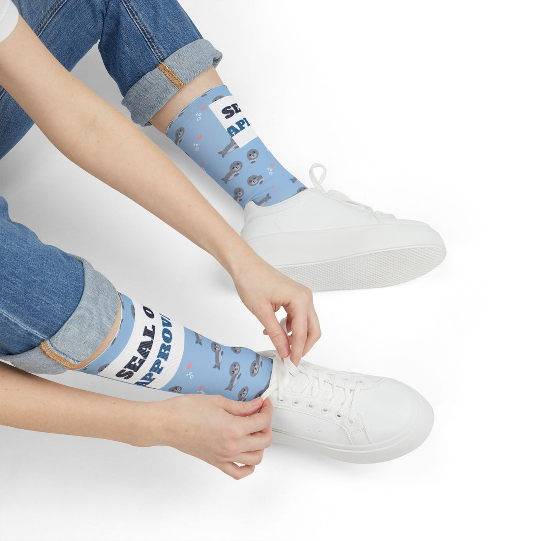 Seated model tying a white sneaker in light blue Seal of Approval Rhode Island socks with gray seals