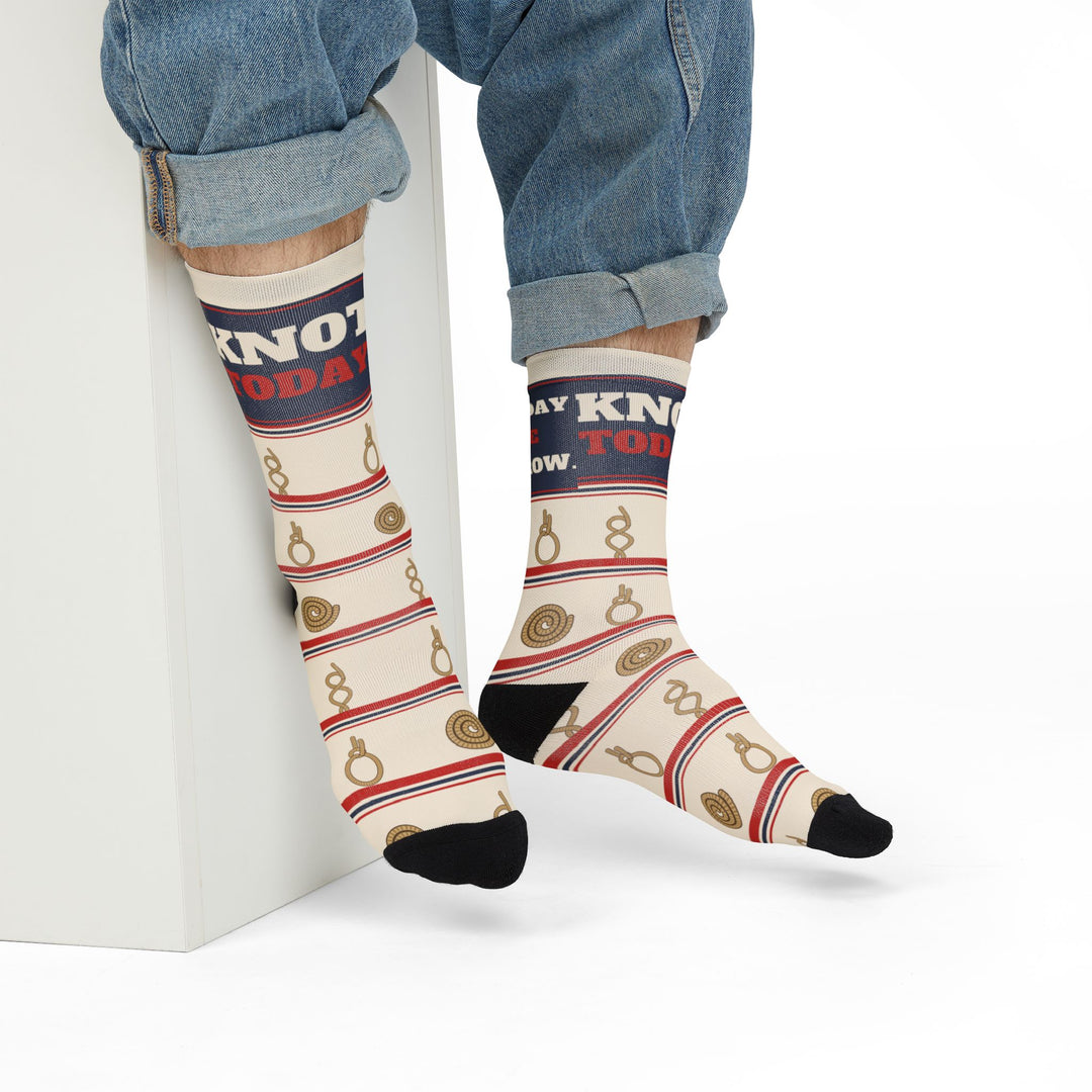 Seated model in rolled jeans on a white block showing Knot Today socks with coiled rope and knot motifs
