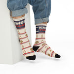 Seated model in rolled jeans on a white block showing Knot Today socks with coiled rope and knot motifs