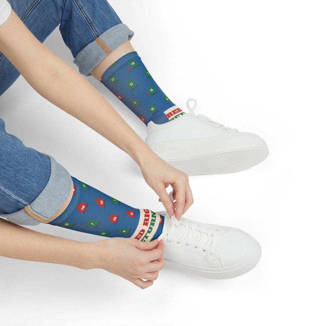 Seated model in jeans tying white sneakers while wearing blue Red Right Returning nautical crew socks