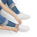 Seated model in jeans tying white sneakers while wearing blue Red Right Returning nautical crew socks