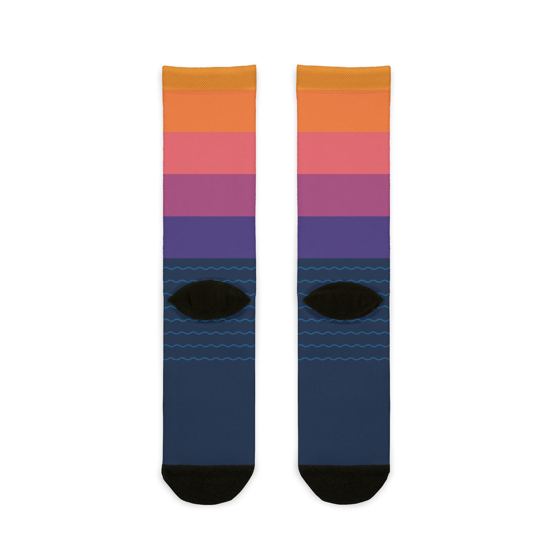 Back flat lay of sunset gradient sailboat socks in orange, pink and purple with navy foot and black heels