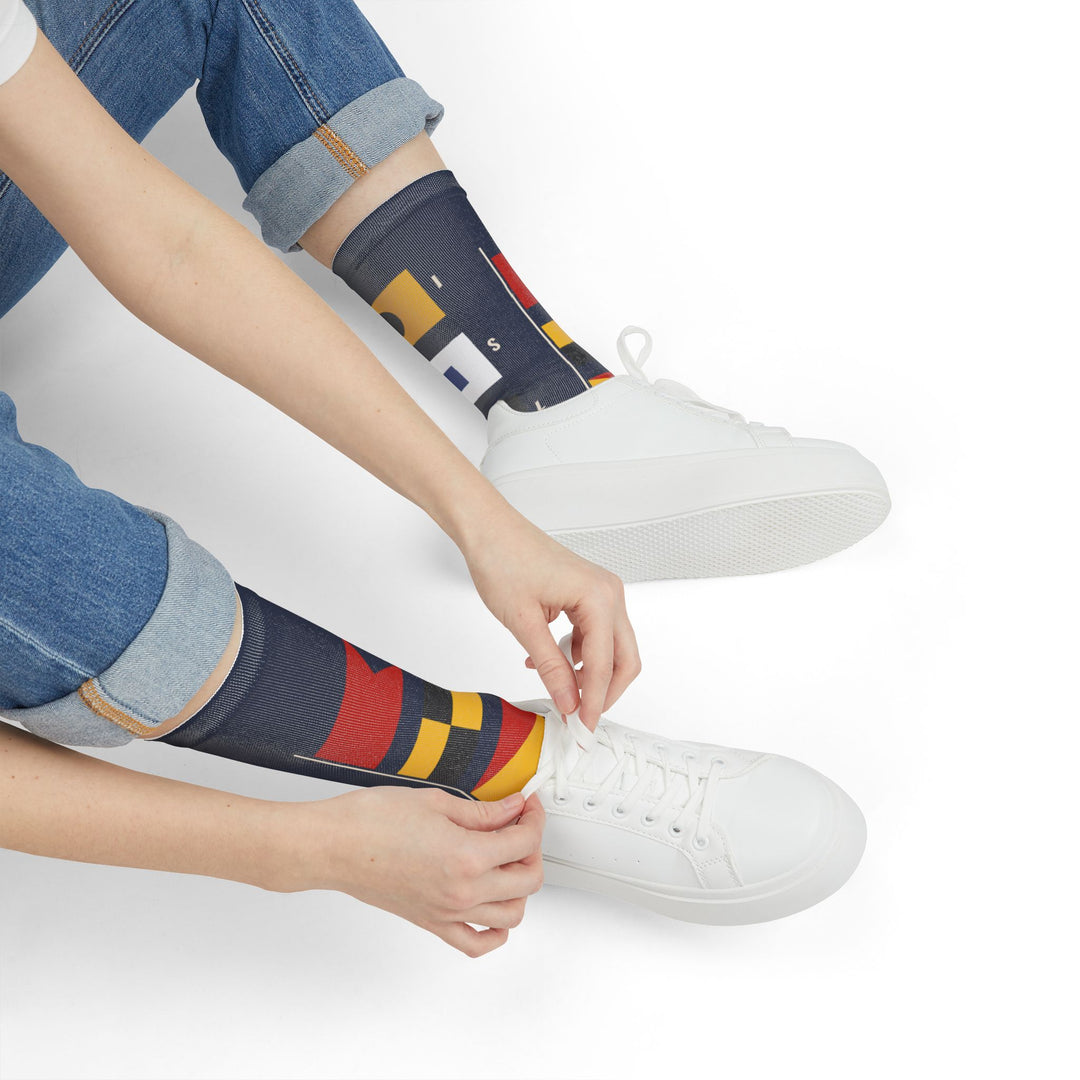 Person in jeans tying white sneakers while wearing navy Block Island signal flag socks