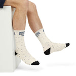 Close side view of raised feet in white Small State. Big Attitude. Rhode Island crew socks with black toes
