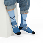 Model in rolled jeans seated on a white block in Whale Hello There socks with the WHALE HELLO THERE slogan