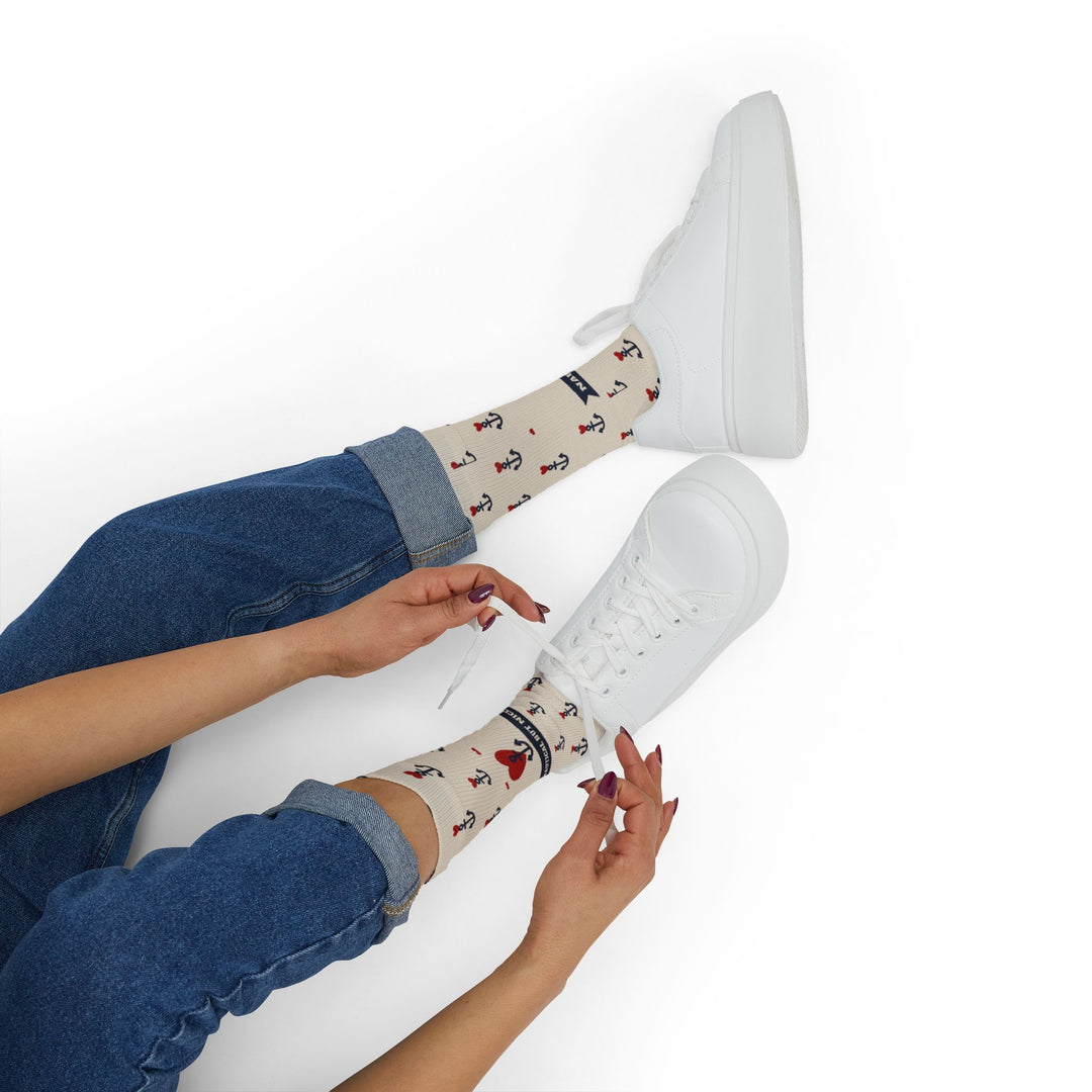 Hands tying white sneakers on a model wearing tan anchor print nautical crew socks with red hearts