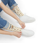 Seated model in rolled jeans and white sneakers pulling on cream Powered by Coffee Milk Rhode Island socks