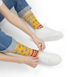 Seated model tying a white sneaker in yellow Swear Like a Sailor funny beach socks with red slogan band