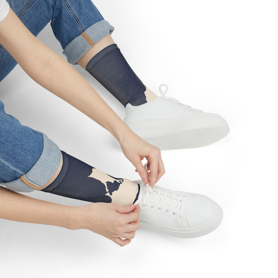 Person in rolled jeans pulling on navy Block Island Outline socks beside white sneakers