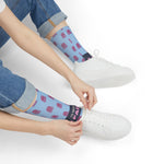 Seated model pulling on light blue I'd Need 4 Pairs octopus socks beside white sneakers