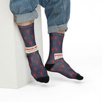 Seated model in rolled jeans leaning on a white block in navy and red lobster Rhode Island socks
