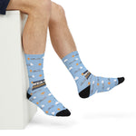 Seated model with crossed legs showing the dark Weather Permitting slogan band on light blue ferry socks