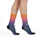 Model standing with crossed feet in orange and purple sunset sailboat socks with navy feet