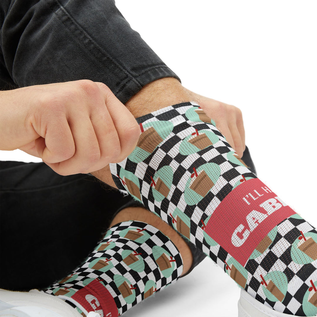 Tight close-up of a hand tugging a checkered sock up the shin, coral I'll Have a Cabinet band on Rhode Island socks