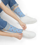 Person in rolled jeans pulling on light blue starfish beach crew socks beside white sneakers