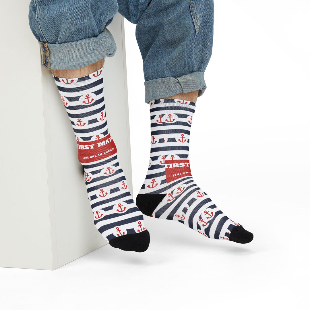 Model in rolled jeans seated on a white block wearing First Mate red anchor stripe funny beach socks