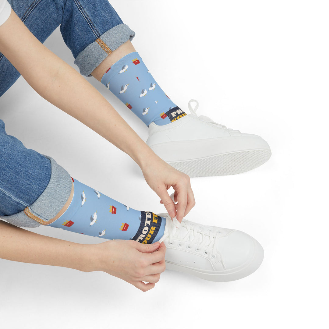 Seated model in jeans tying white sneakers while wearing light blue Protect Your Fries seagull socks