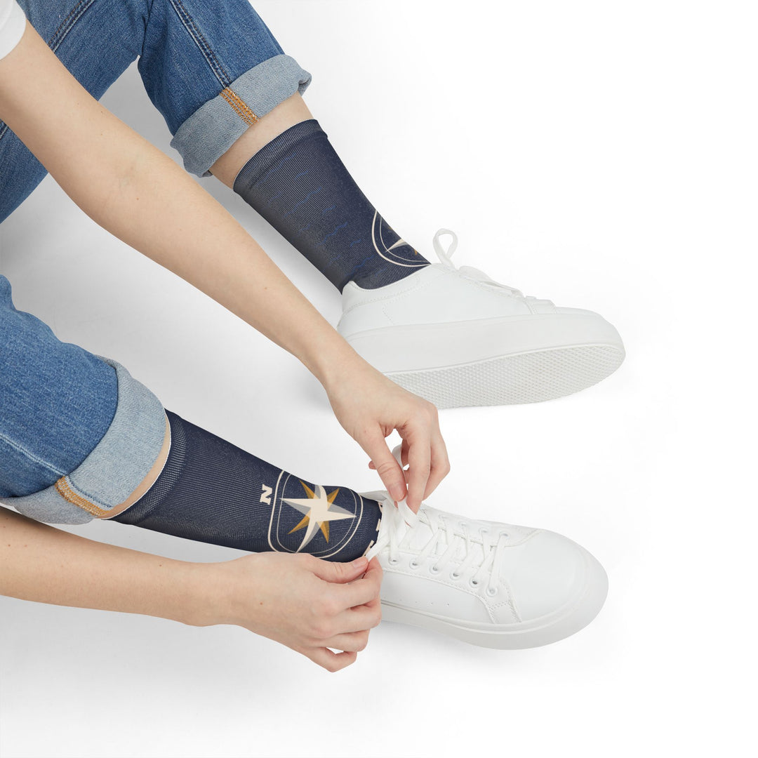 Seated model in jeans tying white sneakers while wearing navy Not Lost, Just Sailing socks