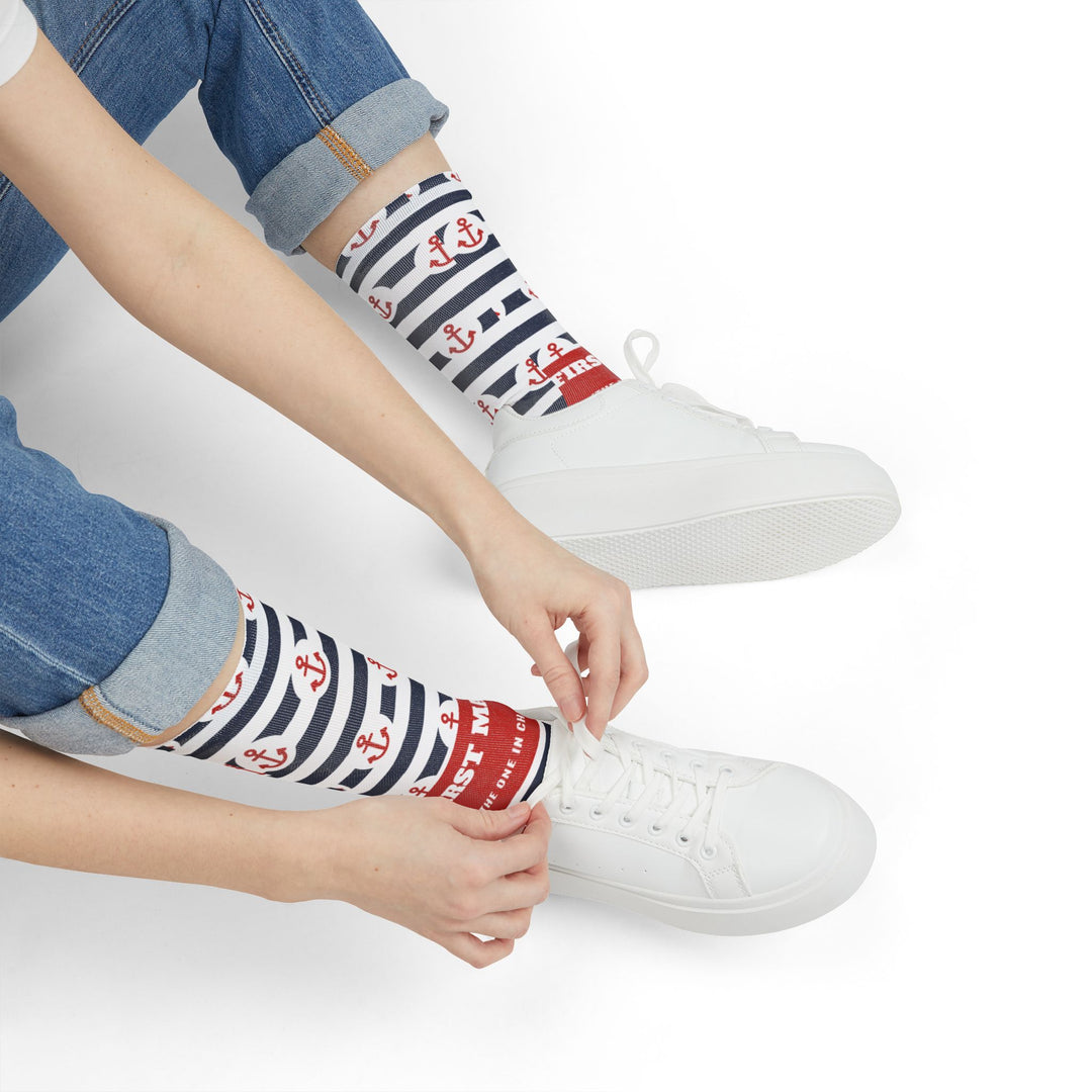 Seated model tying white sneakers while wearing striped First Mate anchor nautical crew socks
