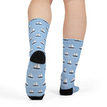 Rear view on a model of light blue nautical socks showing black heel and sailboat print up the calf