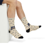 Seated with legs crossed in My Legs Biked the Bluffs Block Island socks, bicycle print and black toes