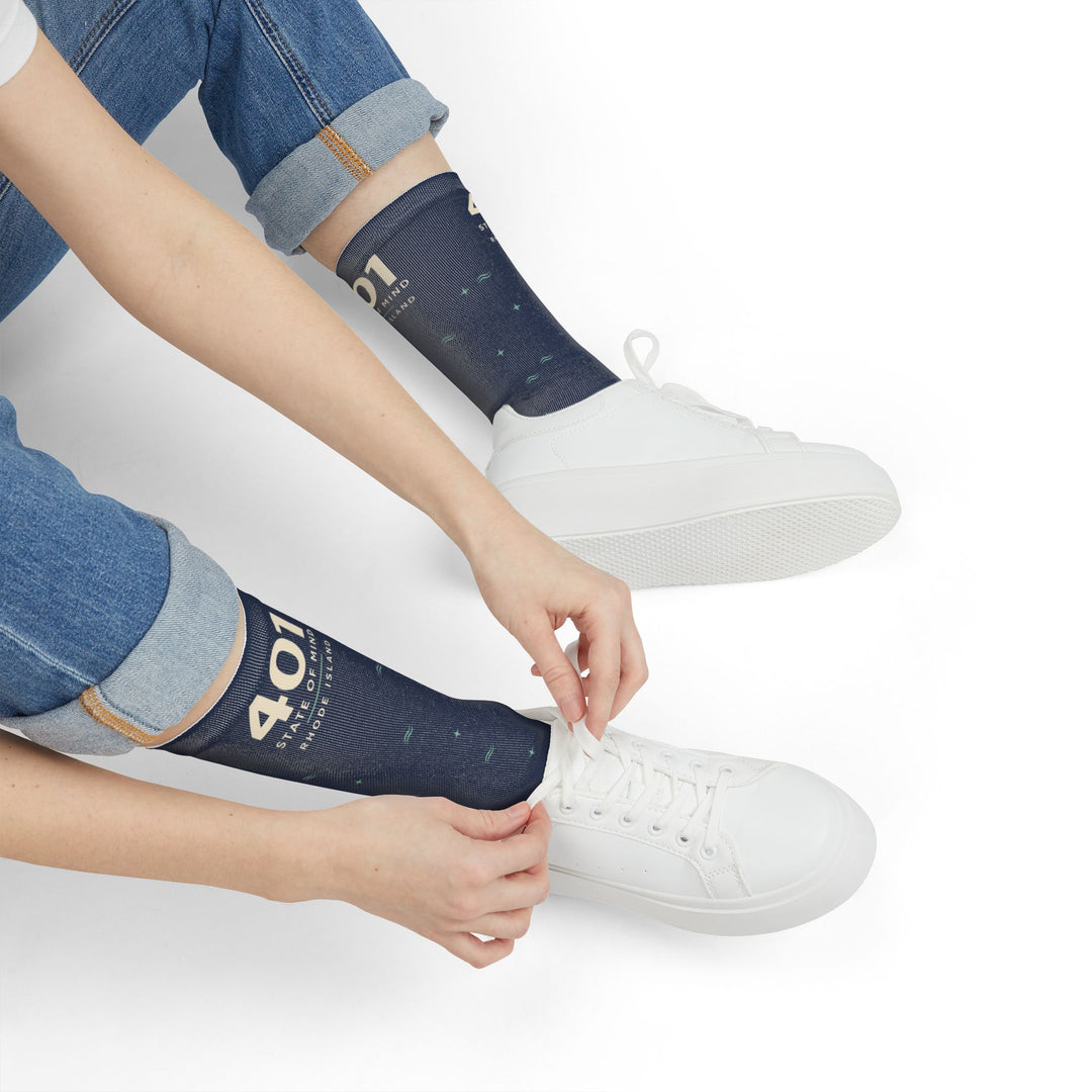 Seated model in rolled jeans and white sneakers pulling up navy 401 State of Mind Rhode Island socks