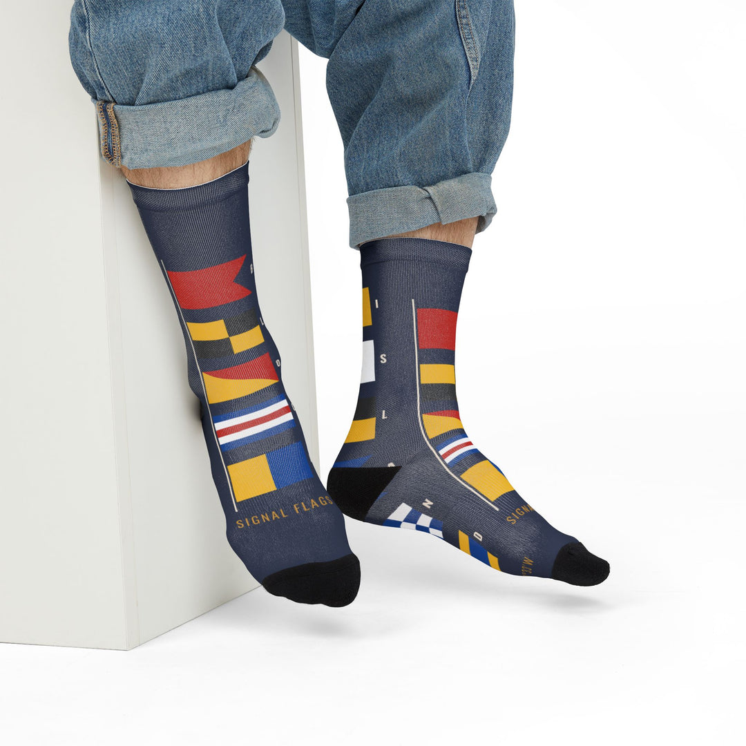 Model in rolled jeans seated on a white block wearing BLOCK ISLAND nautical flag crew socks