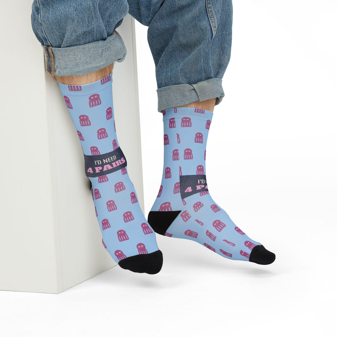 Model in rolled jeans seated on a white block wearing light blue I'd Need 4 Pairs octopus socks