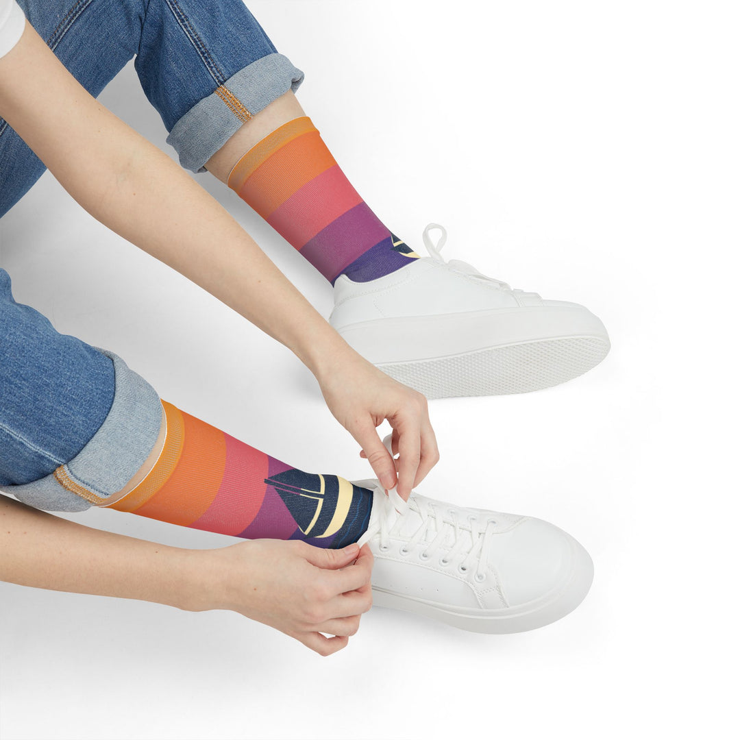 Seated model tying white sneakers while wearing sunset fade nautical crew socks with sailboat graphic