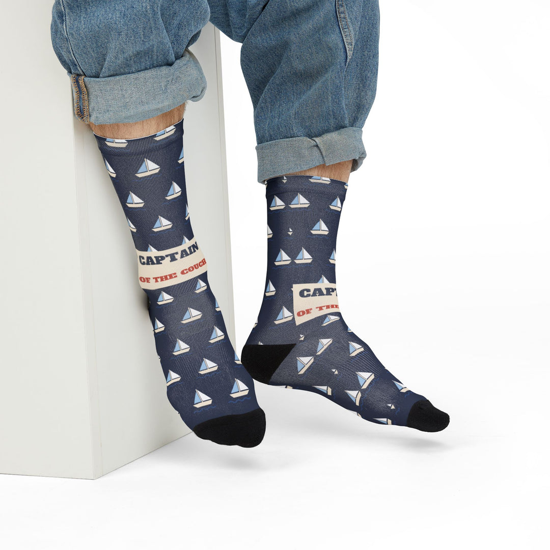 Seated model in rolled jeans on a white block showing navy Captain of the Couch sailboat crew socks