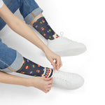 Seated model in rolled jeans pulling on white sneakers over navy Nice Buoys lobster buoy crew socks