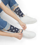 Seated model tying a white sneaker while wearing navy Captain of the Couch funny sailboat socks