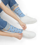 Model in jeans and white sneakers pulling on light blue Sailboat Regatta socks with white sails