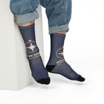 Seated model in rolled jeans leaning on a white block showing the compass rose on navy nautical crew socks
