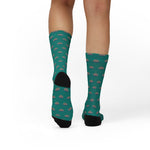 Back view of a standing model in teal Quahog Squad funny beach socks, black heels and clam print up to the calf