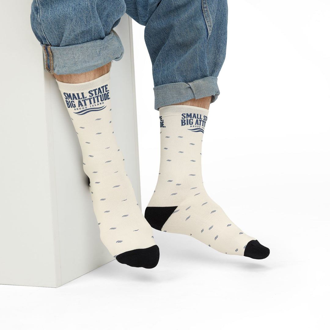 Model in rolled jeans seated on a white block wearing Small State. Big Attitude. funny Rhode Island socks