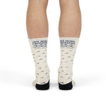 Standing legs in off-white Block Island socks showing the One More Crossing navy wave logo on the shins