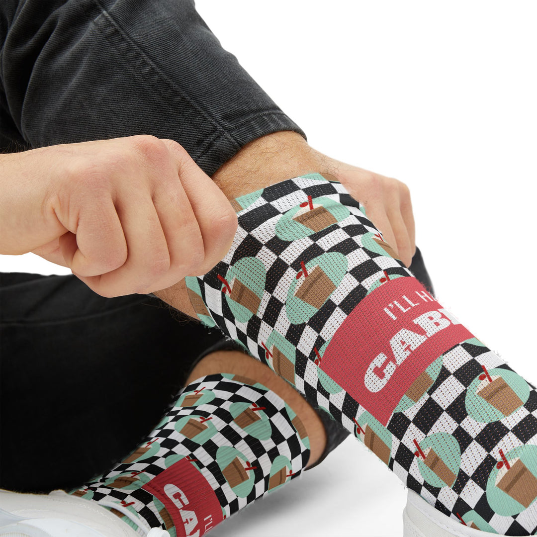 Close-up of hands pulling up a checkered sock showing the coral I'll Have a Cabinet band, Rhode Island coffee cabinet socks