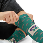 Tight close-up of a hand tugging a teal clam sock up the shin, purple Quahog Squad lettering on Rhode Island socks