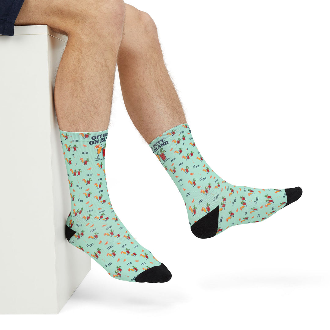 Crossed legs in mint green funny beach socks with cocktail, orange slice and navy wave print, side view