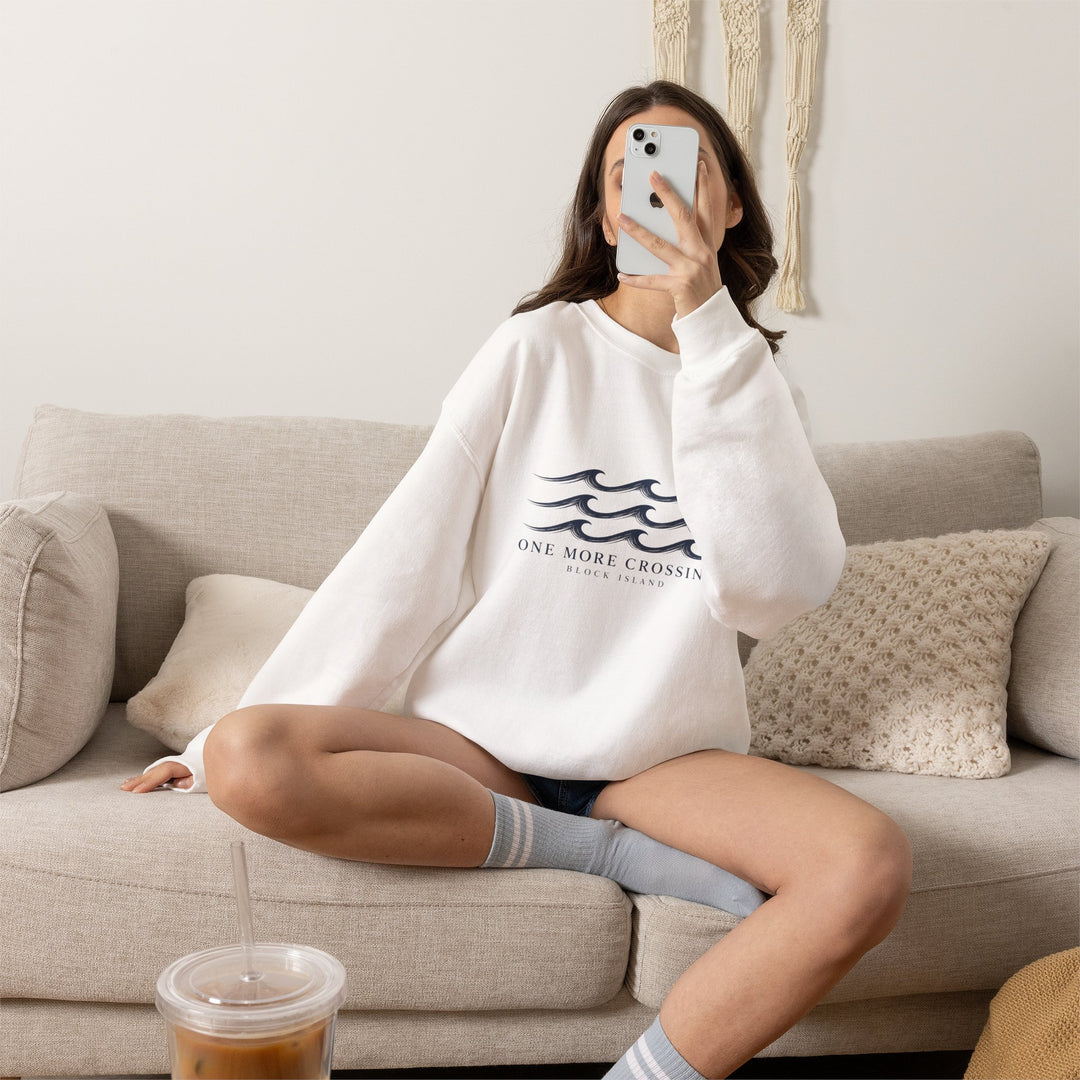 Model curled on a sofa with her phone wearing the white One More Crossing Rhode Island sweatshirt