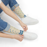 Model in jeans and white sneakers pulling on Sea Glass Hunter crew socks, a gift for beachcombers